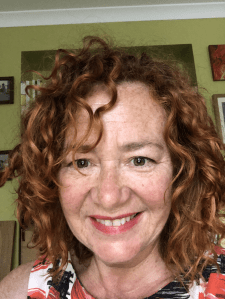A photograph of Annamarie taken as a head shot, she is looking directly at the camera. She has wavy auburn hair and is smiling.