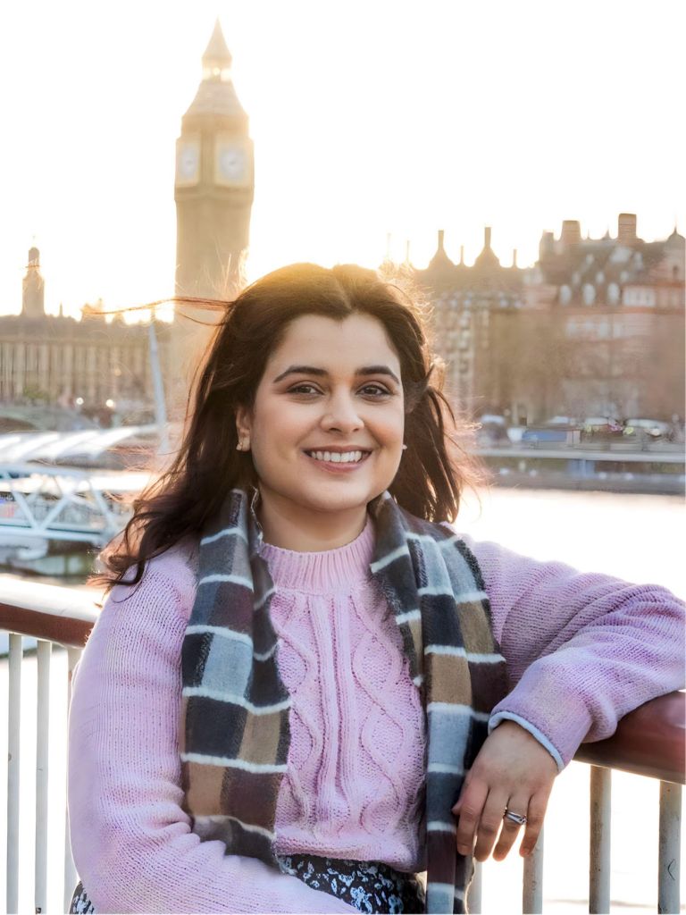 Profile picture of Kelly Trivedy sitting by the Thames on the opposite bank to Parliament with the Elizabeth Tower in the background.