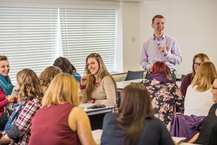 Image of a class with people on group tables discussing and all smiling and laughing.